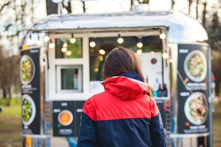 Girl choosing and ordering street food in colourful food truck van on a festival in a city park,...