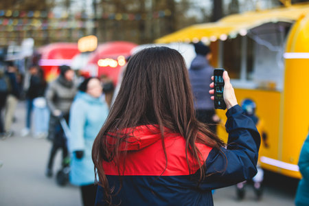 Girl choosing and ordering street food in colourful food truck van on a festival in a city park, summer sunny day, food stall kiosk offers fast food, coffee and drinks for sale, food court outdoorsの写真素材