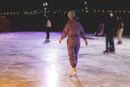 Girl skating on the ice rink arena with happy people around, concept of ice skating in winter, winter activities, holiday christmas time, with new year decoration and illuminationの写真素材