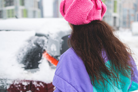 Process of cleaning a car from snow in the morning, girl removing snow from windscreen with a window...