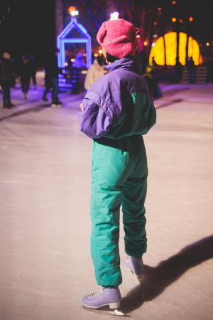Girl skating on the ice rink arena with happy people around, concept of ice skating in winter, winter activities, holiday christmas time, with new year decoration and illuminationの写真素材