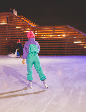 Girl skating on the ice rink arena with happy people around, concept of ice skating in winter, winter activities, holiday christmas time, with new year decoration and illuminationの写真素材