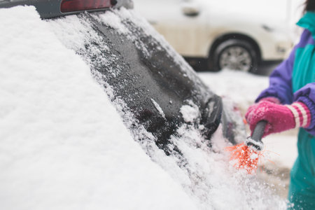 Process of cleaning a car from snow in the morning, girl removing snow from windscreen with a window...