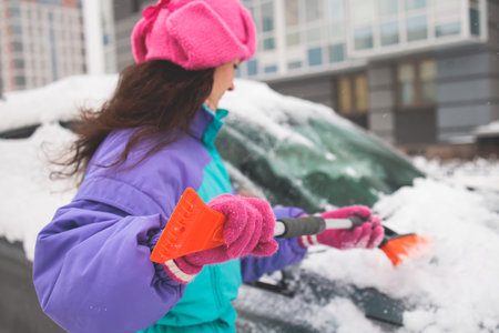 Process of cleaning a car from snow in the morning, girl removing snow from windscreen with a window...