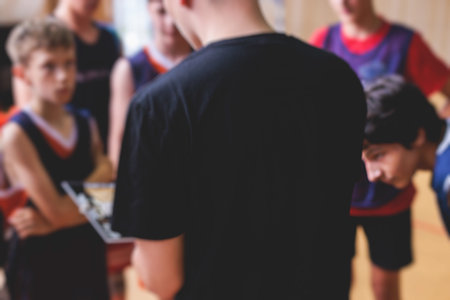Junior young basketball team with a coach, group of kids children team having training and team talk speach with trainer instructor, basket coach explaining the game plan tactics on a clipboardの写真素材