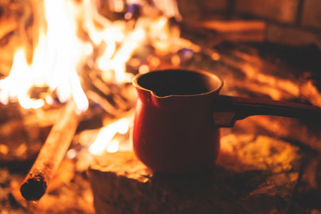 Warming up the fire, cozy winter night in the scandinavian cottage house cabin by the fireplace, burning fire with charcoal and firewood, heating up the drink beverage in a coffee potの写真素材