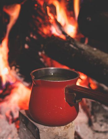 Warm by the fire, cozy winter night in the scandinavian cottage house cabin by the fireplace, burning fire with charcoal and firewood, heating up the drink beverage, tea or soup in coffee potの写真素材