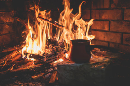 Warming up the fire, cozy winter night in the scandinavian cottage house cabin by the fireplace, burning fire with charcoal and firewood, heating up the drink beverage in a coffee potの写真素材