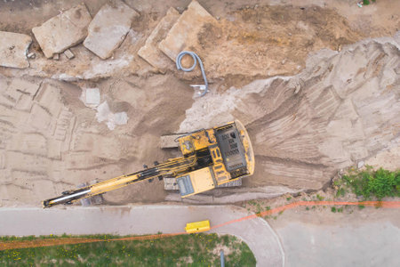 Yellow heavy excavator excavating sand and working during road works, unloading sand during construction of a new road, aerial drone top viewの写真素材
