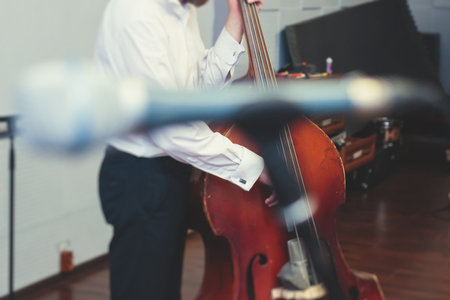 Contrabass cellist player in headphones during rehearsal, recording sound for new album song at studio, cello violoncellist musician with microphone and a musical band orchestra, music productionの写真素材