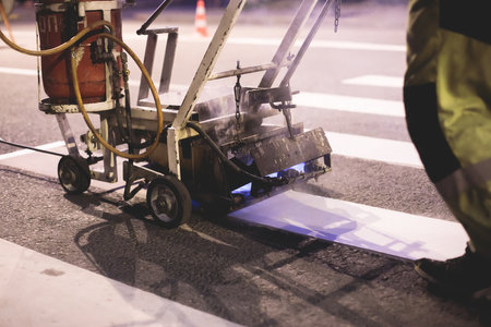 Process of making new road surface markings with a line striping machine, workers improve city infrastructure, demarcation marking of pedestrian crossing with hot melted paint on asphalt pavementの写真素材