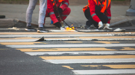 Process of making new road surface markings with a line striping machine, workers improve city infrastructure, demarcation marking of pedestrian crossing with a hot melted paint on asphalt pavementの写真素材