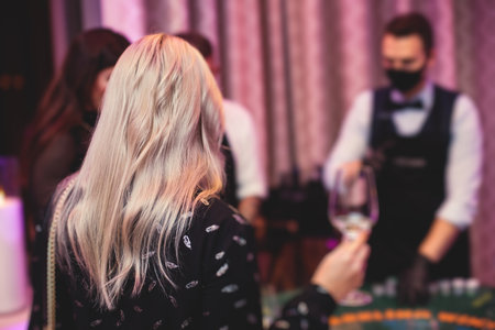 Casino concept, casino table with roulette in motion, with casino chips, tokens, the hand of croupier, dollar bill money and a group of gambling rich wealthy people playing bet in a backgroundの写真素材