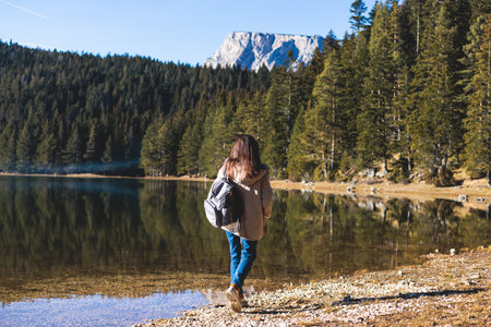 Beautiful view of Black lake, Crno Jezero in Durmitor National Park, Zabljak, northern Montenegro, with a female tourist, landscape in sunny day with blue sky, forest hiking trail and mountainsの写真素材