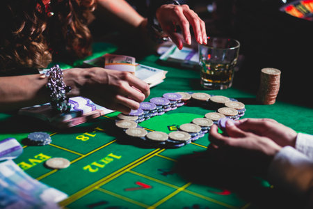 A close-up vibrant image of multicolored casino table with roulette in motion, with casino chips. the hand of croupier, mone and a group of gambling rich wealthy people in the backgroundの写真素材
