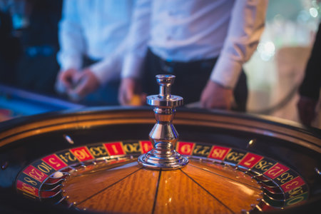 A close-up vibrant image of multicolored casino table with roulette in motion, with the hand of croupier, and a group of gambling rich wealthy people in the backgroundの写真素材