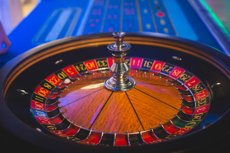 A close-up vibrant image of multicolored casino table with roulette in motion, with the hand of croupier, and a group of gambling rich wealthy people in the backgroundの写真素材