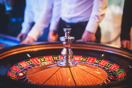A close-up vibrant image of multicolored casino table with roulette in motion, with casino chips. the hand of croupier, mone and a group of gambling rich wealthy people in the backgroundの写真素材