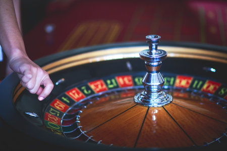 A close-up vibrant image of multicolored casino table with roulette in motion, with casino chips. the hand of croupier, mone and a group of gambling rich wealthy people in the backgroundの写真素材