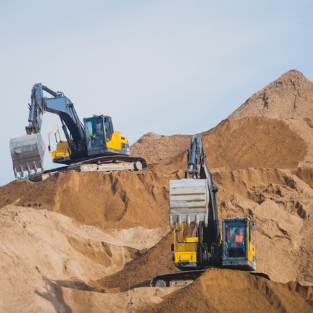 Yellow heavy excavator excavating sand and working during road works, unloading sand during construction of the new roadの写真素材