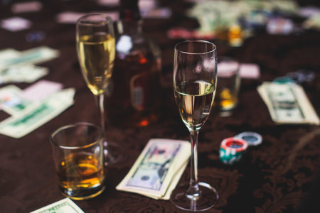 View of poker table with pack of cards, tokens, alcohol drinks, dollar money and group of gambling...