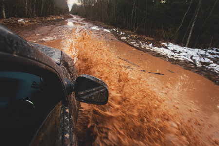Suv offroad 4wd car rides through muddy puddle, off-road track road, with a big splash, during a...
