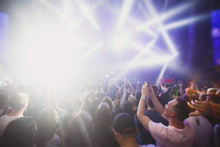 A crowded concert hall with stage stage lights, rock show performance, with people silhouettes...