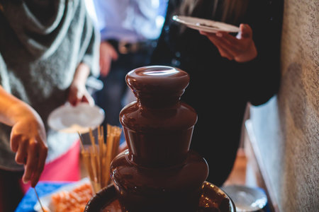 Vibrant Picture of Chocolate Fountain Fontaine on a children kids birthday party with a kids playing around and dipping marshmallows and fruits into the fountainの写真素材