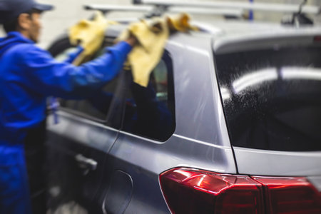Process of washing the silver gray car in the carwash, concept of manual car wash with pressurized water, worker washing car's alloy wheels on a car wash, detail view of wash foam water.の写真素材