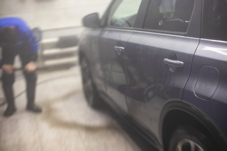 Process of washing the silver gray car in the carwash, concept of manual car wash with pressurized water, worker washing car's alloy wheels on a car wash, detail view of wash foam water.の写真素材