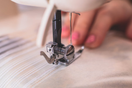 Process of sewing the curtains at home, close up of curtain tape on the sewing machine, hemming, tailoring, repairing and stitching cloth and dress, with the hand of female dressmaker in backgroundの写真素材