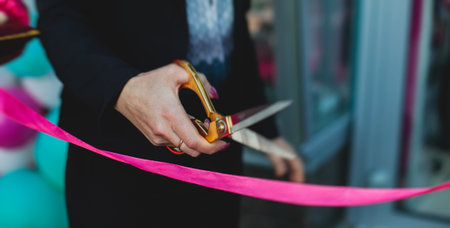 Process of cutting the red ribbon during the grand opening of the new shopping center mall building, opening of exhibition, close up view of red ribbon with people aroundの写真素材