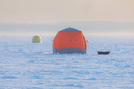 Process of ice fishing, group of fishermen on ice near tent shelter, with equipment in a winter snowy day, tents and ice auger on a frozen lakeの写真素材
