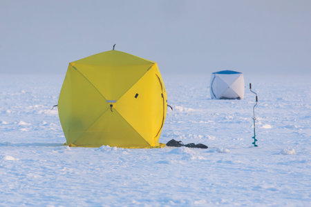 Process of ice fishing, group of fishermen on ice near tent shelter, with equipment in a winter...
