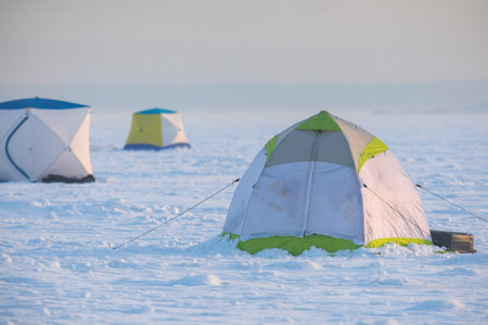 Process of ice fishing, group of fishermen on ice near tent shelter, with equipment in a winter...
