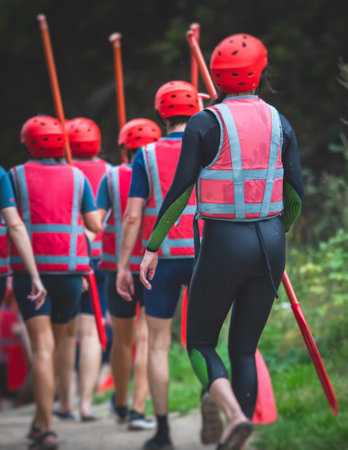 Group of sportsmen in wetsuits with paddles in helmets and life jackets vest prepare to extreme water sports, team before rafting, kayaking, canoeing in summer day, equipment view with raft boatの写真素材