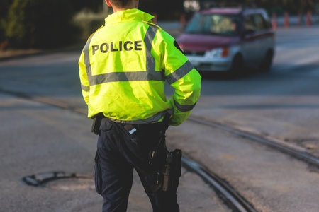 Inspector of traffic police highway patrol regulates the movement of transport in the center of European city, in green yellow vest jacket with sign "Police", police officer control road trafficの写真素材
