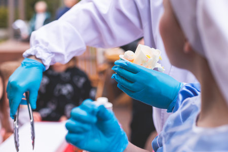 Rolled thai ice cream preparation, process of cooking colored fried ice cream at frozen pan, cooking class on kids child birthday party celebration with happy children aroundの写真素材