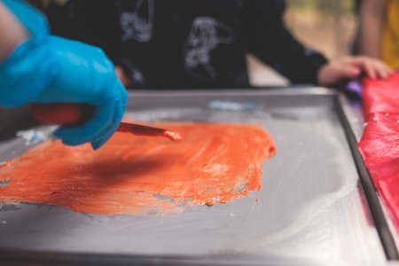 Rolled thai ice cream preparation, process of cooking colored fried ice cream at frozen pan, cooking class on kids child birthday party celebration with happy children aroundの写真素材
