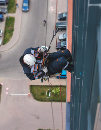 Professional climber rope access worker painting, repairing and cleaning windows on facade of...