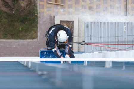Professional climber rope access worker painting, repairing and cleaning windows on facade of residential skyscraper high rise building exterior wall, industrial mountaineers working at heightsの写真素材