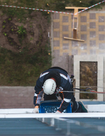 Professional climber rope access worker painting, repairing and cleaning windows on facade of residential skyscraper high rise building exterior wall, industrial mountaineers working at heightsの写真素材