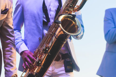 Concert view of saxophonist in a blue and white suit, a saxophone sax player with vocalist and musical band during jazz orchestra show performing music on stage in scene lightsの写真素材
