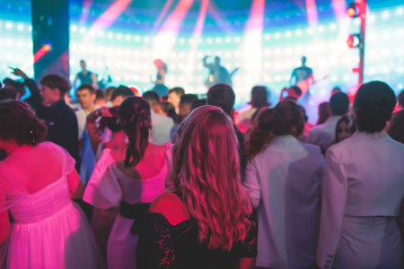 A crowded concert hall arena with scene stage lights with musicians band on a stage at the venue, rock show performance, with concert-goers attendees, audience on dance floor during concert festivalの写真素材