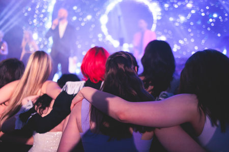 A crowded concert hall arena with scene stage lights with musicians band on a stage at the venue, rock show performance, with concert-goers attendees, audience on dance floor during concert festivalの写真素材