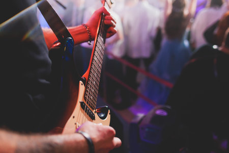 Concert view of an electric guitar player with vocalist and rock band performing in club, male musician guitarist on stage with audience in a crowded concert hall arenaの写真素材