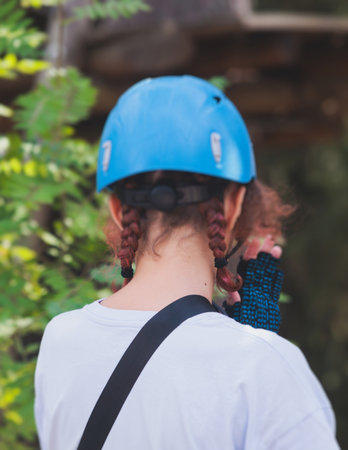 View of high ropes course, kids of climbing in amusement activity rope park, passing obstacles and zip line on heights, children teenagers in equipment gear between the trees on heights, summer dayの写真素材