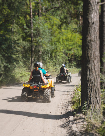 Group of riders riding ATV vehicle crossing forest rural road, process of driving a rental vehicle, all terrain quad bike vehicle, during off-road tour adventure competition in a summer sunny dayの写真素材