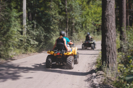 Group of riders riding ATV vehicle crossing forest rural road, process of driving a rental vehicle, all terrain quad bike vehicle, during off-road tour adventure competition in a summer sunny dayの写真素材