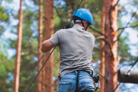 View of high ropes course, process of climbing in amusement acitivity rope park, passing obstacles and zip line on heights in climbing safety equipment gear between the trees om heights in summer dayの写真素材